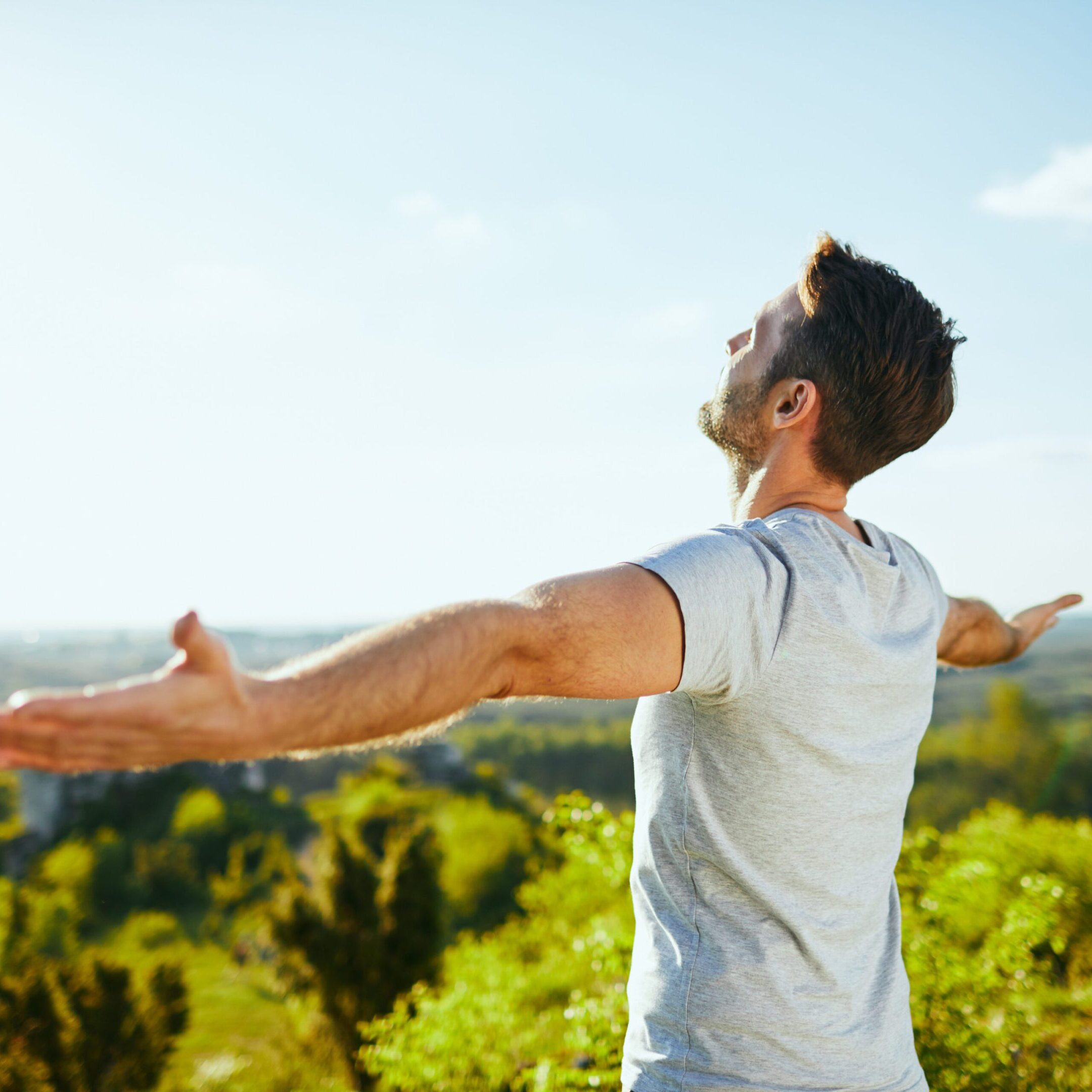 Man extending arms and admiring the view on sunny day in a forest